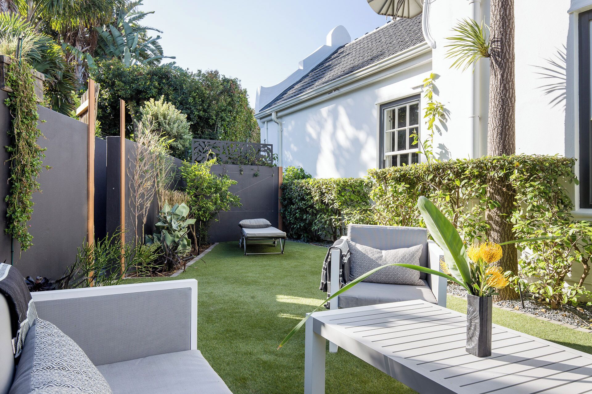 A well-maintained garden with a white outdoor seating area, a small table, and a variety of plants and shrubs.