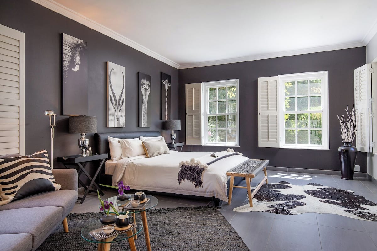 A modern bedroom with a bed, bedside tables, a glass coffee table, and a large window with shutters.