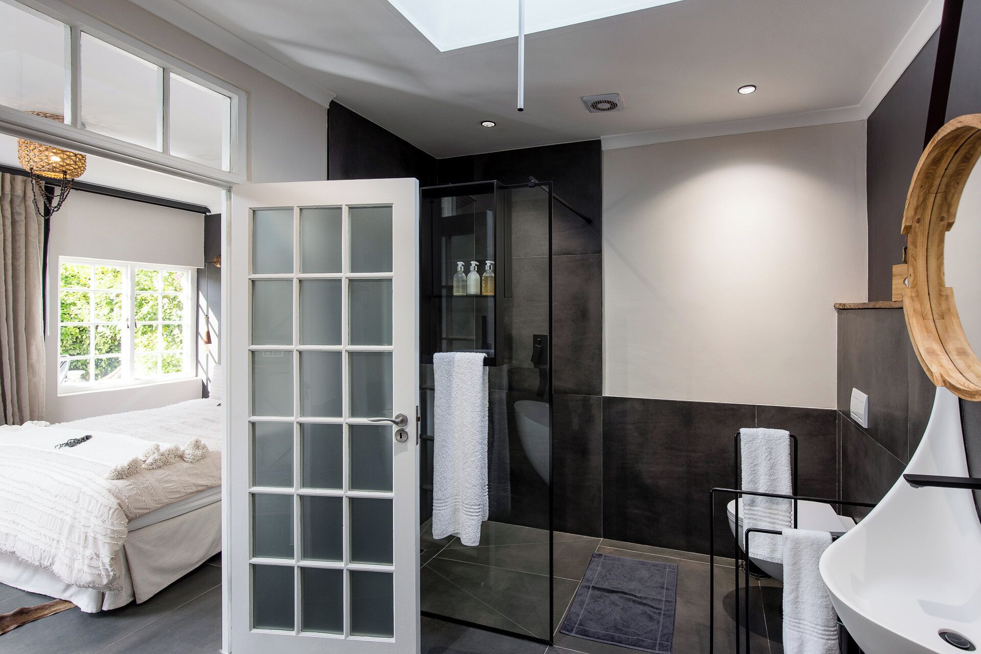 A modern bathroom with a glass shower enclosure, a large mirror, and a white bathtub.