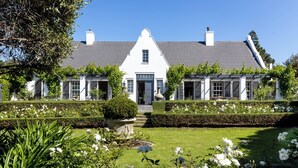 Una casa bianca con tetto grigio, circondata da giardini e siepi curati.