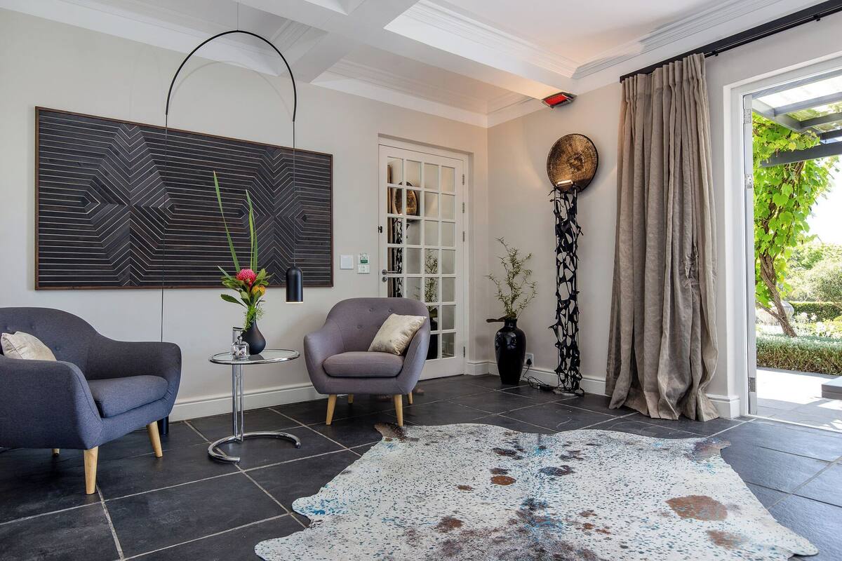 A modern living room with a large abstract painting, a grey sofa, a round table with a vase, and a patterned rug.