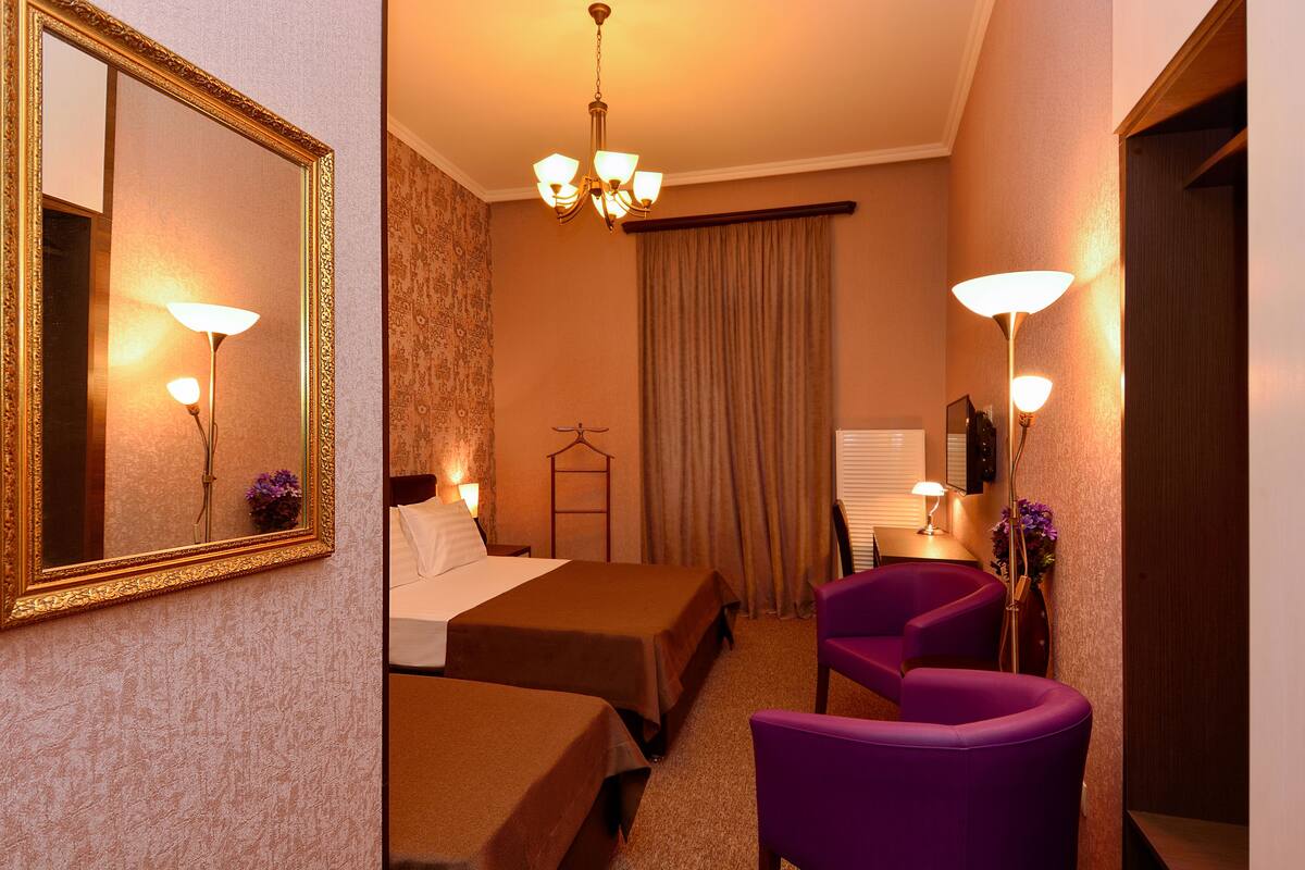 A hotel room with two beds, a chandelier, a mirror, and purple chairs.