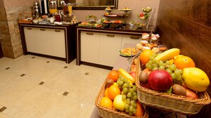 A buffet setup with various food items and a fruit basket. - Hotel King David (Tbilisi)