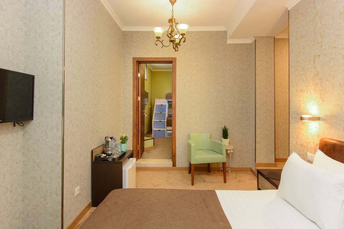 A hotel room with a bed, a television, a small desk with a lamp, and a chair.