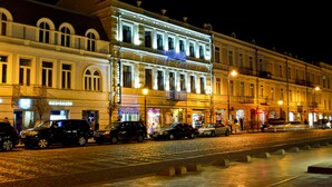 A row of historic buildings with illuminated facades, a cobblestone street, and parked cars. - Hotel King David (Tbilisi)
