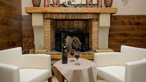 A cozy room with a fireplace, white leather chairs, a table with a bottle and glasses, and decorative items on the mantel. - Hotel King David (Tbilisi)