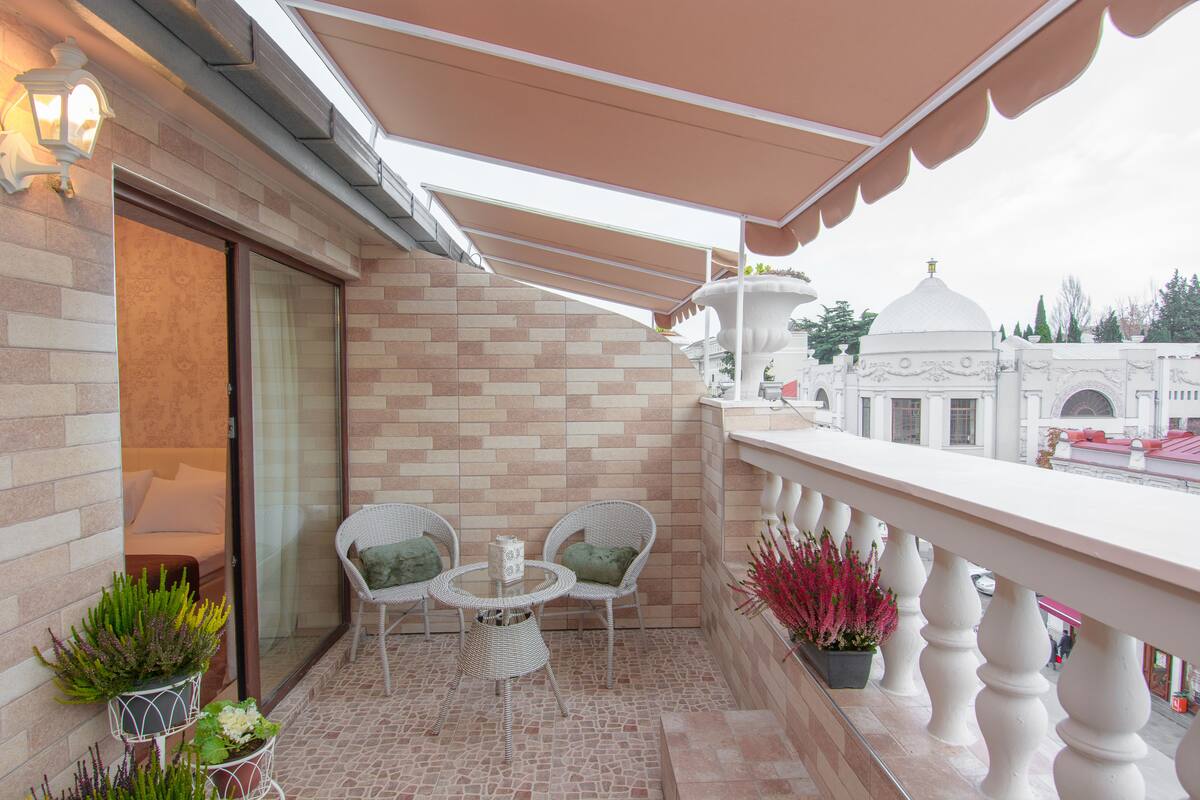 A balcony with wicker chairs and a small table, a potted plant, and a view of a building with a dome.