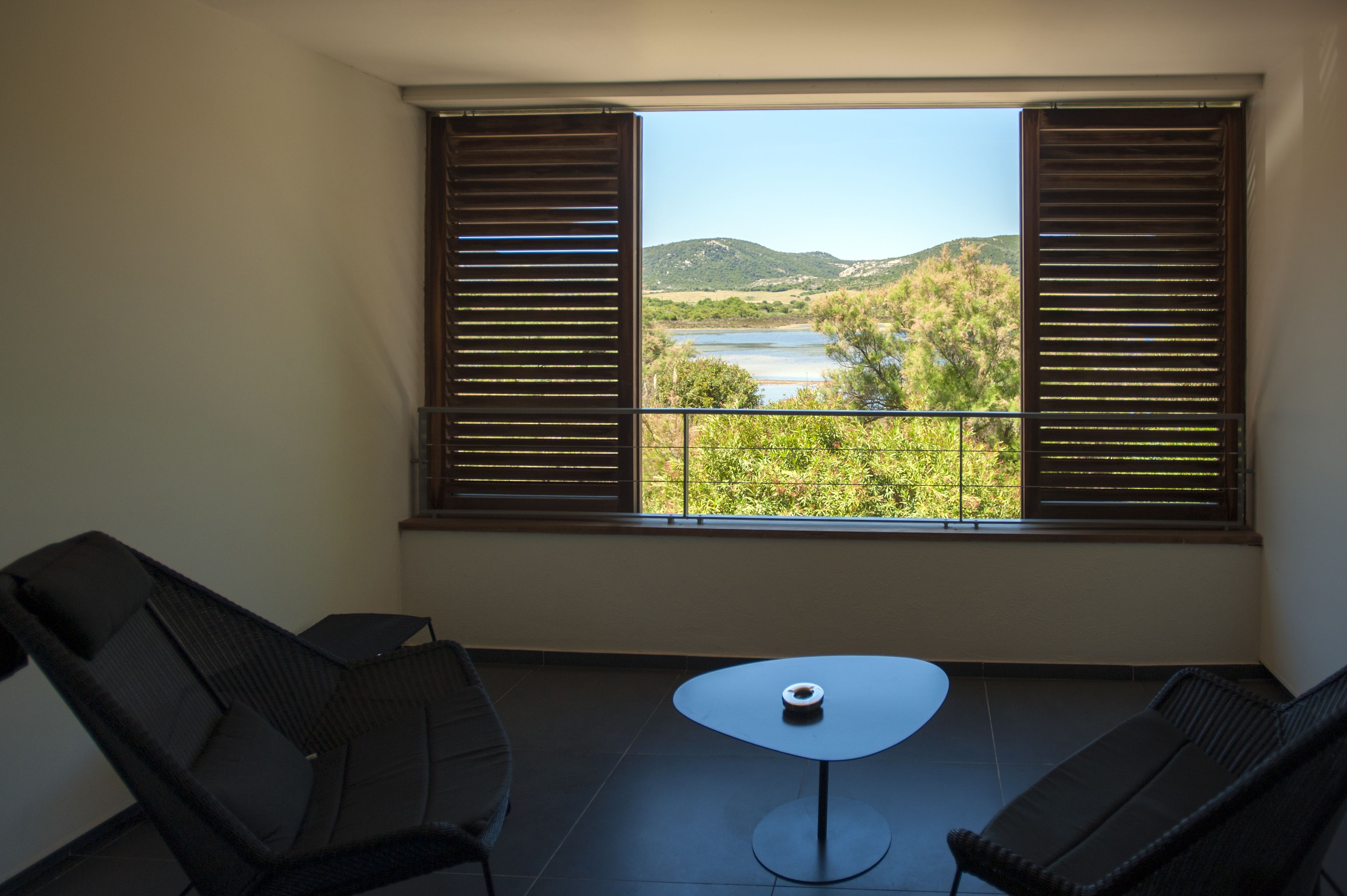 A balcony with two chairs and a small table, overlooking a river and hills.