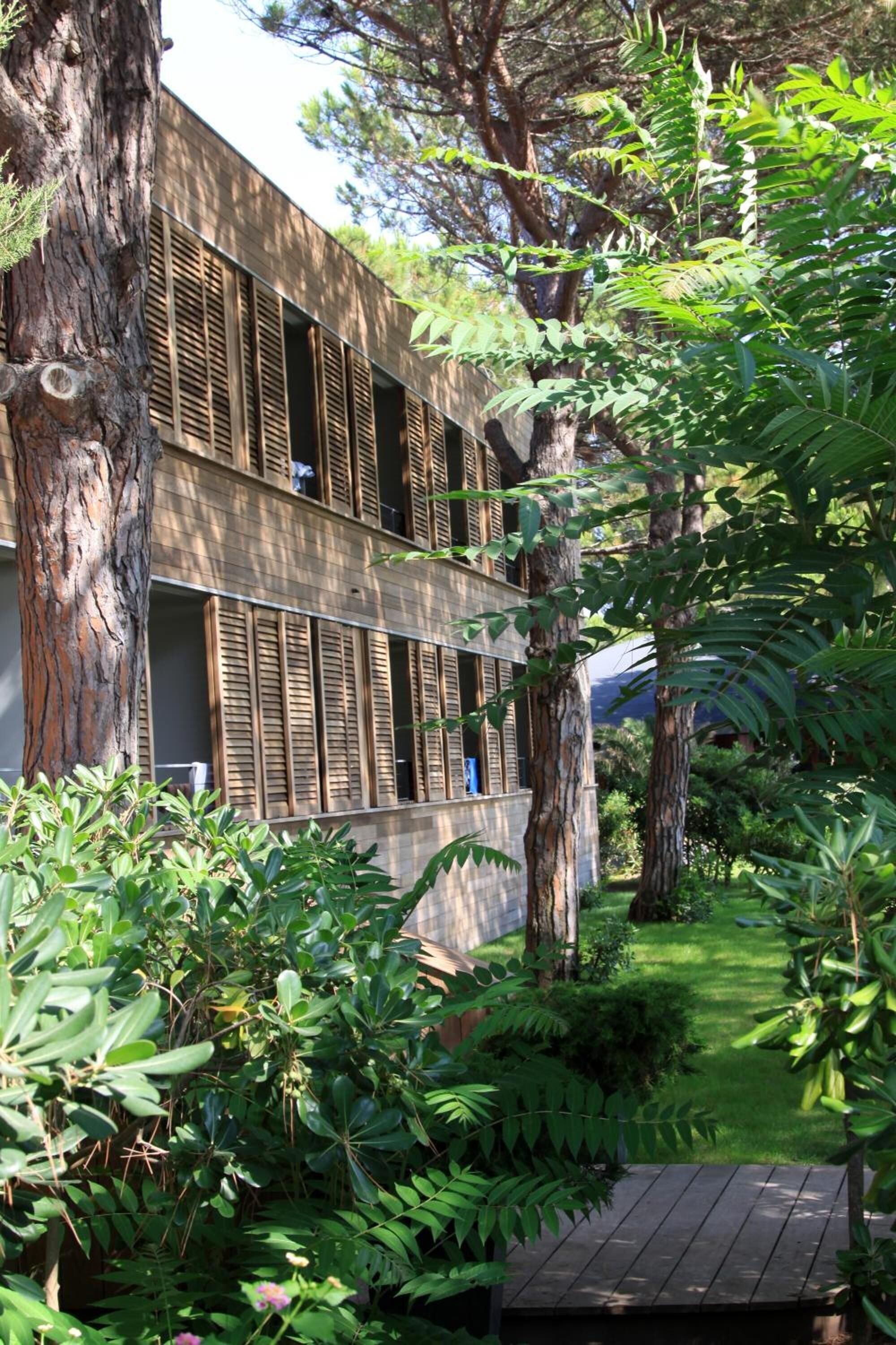 Un edificio de diseño moderno, con contraventanas de madera y un jardín exuberante con diversas plantas y árboles.