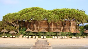 Ein Holzhaus mit Strand davor, umgeben von Bäumen und Sonnenschirmen.