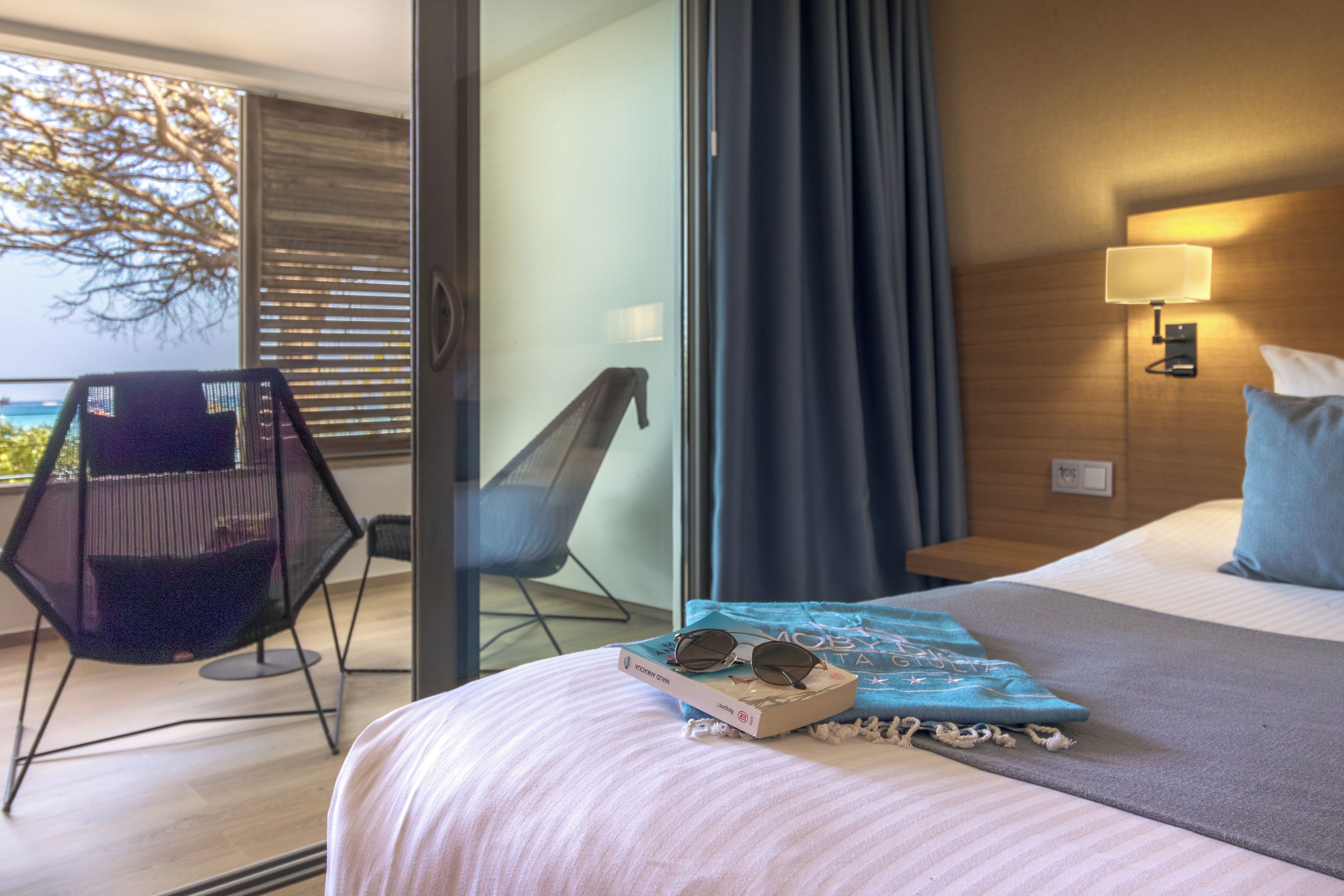 A hotel room with a bed, a chair, a table, and a view of the outdoors.