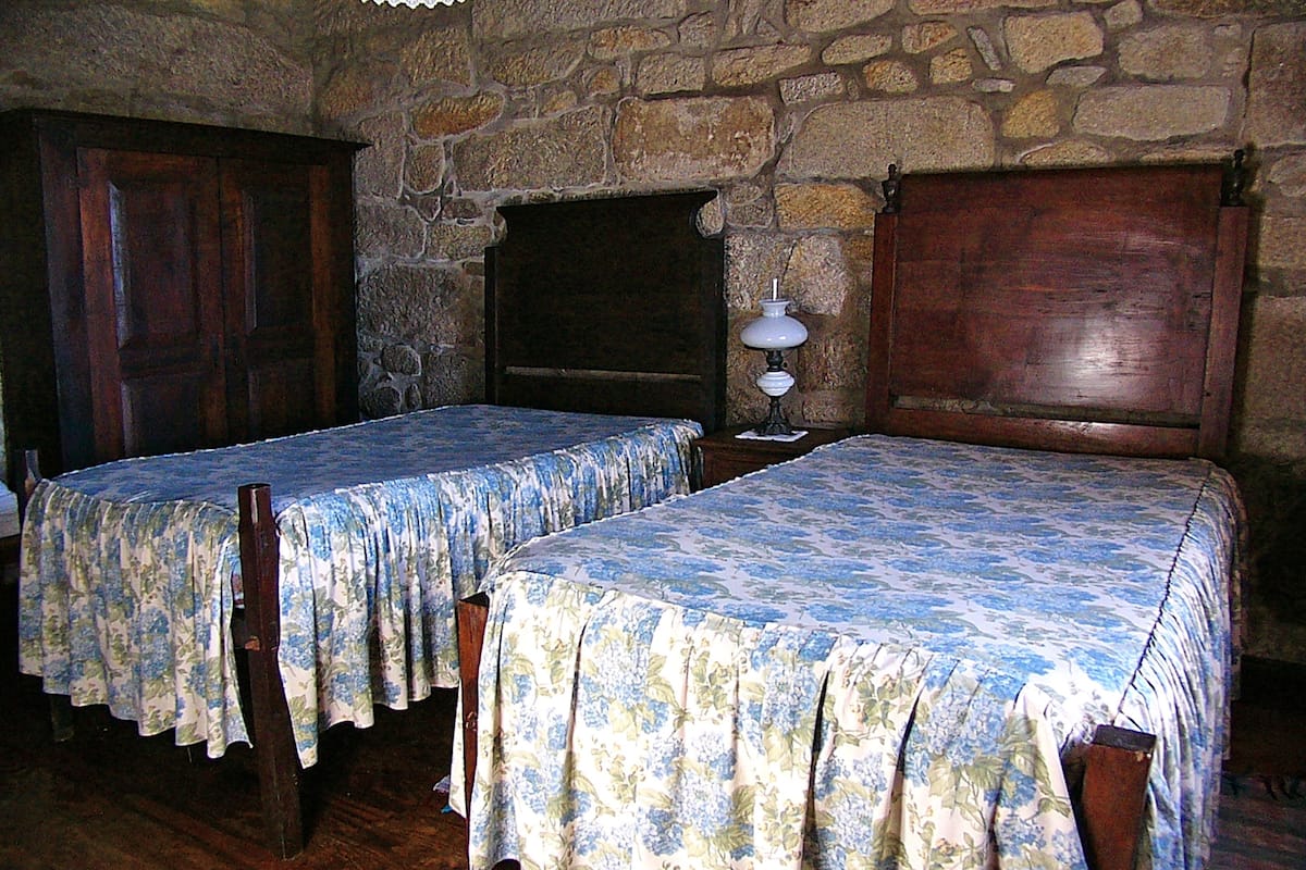 A room with two wooden beds with floral bedspreads, a stone wall, and a wooden door.