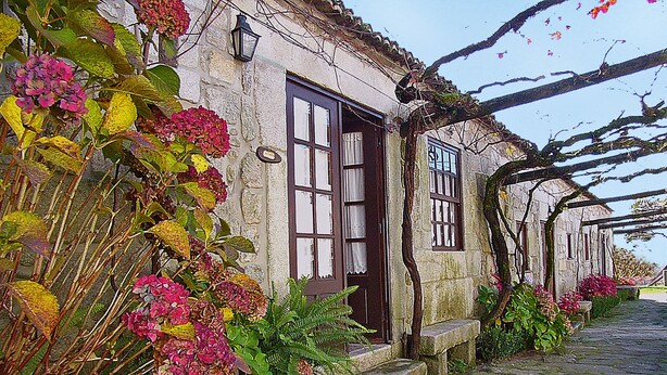 Un edificio de piedra con una puerta de madera oscura, una ventana con cortina blanca y un muro de piedra.