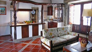 Una cocina rústica con un banco de madera, piso de baldosas y vistas al exterior a través de una ventana.