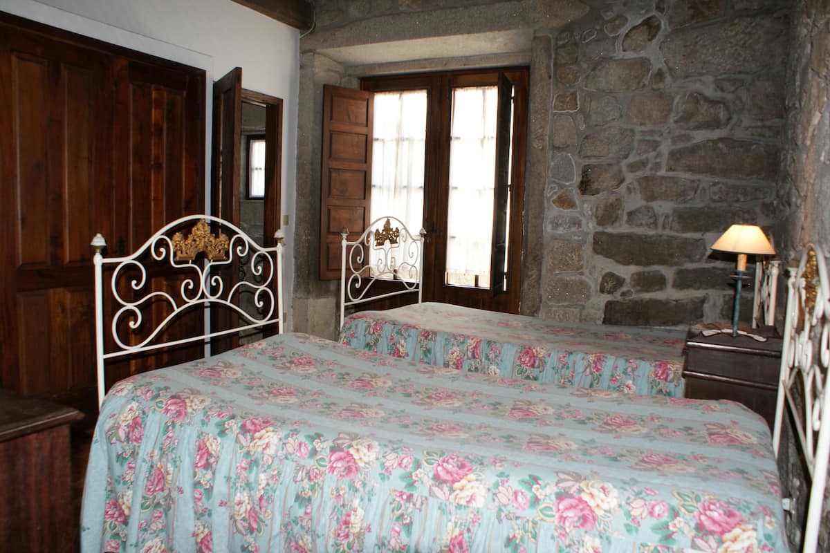A bedroom with two beds, wooden wardrobe, stone wall, and a window with wooden shutters.