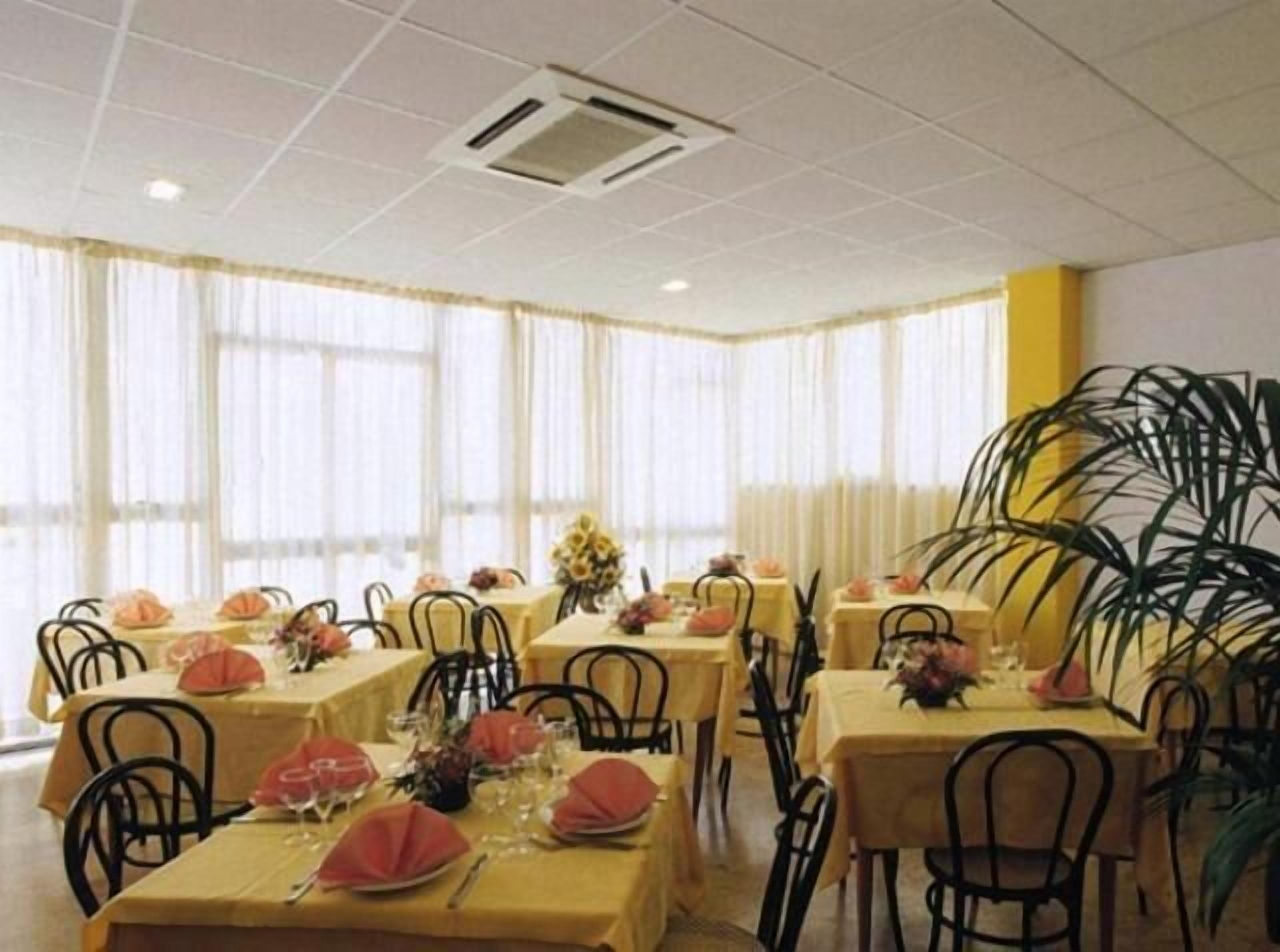 Un espace repas avec des tables dressées pour quatre personnes, chacune étant recouverte d’une nappe jaune, entourée de chaises noires et agrémentée de serviettes rouges.