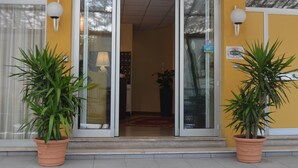 A building entrance with a glass door, a number '19' above it, and two potted plants on either side. - Hotel Capitol (Pesaro)