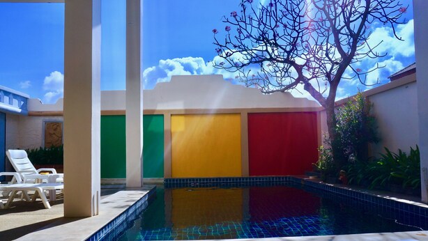 A swimming pool with a tiled edge, surrounded by white lounge chairs, and a tree with sparse foliage. - Rasta Hotel (Koh Samui)