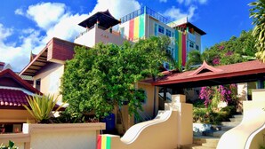 A multi-story building with a colorful facade, a staircase with a curved design, and surrounding greenery. - Rasta Hotel (Koh Samui)