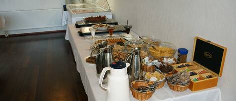 A buffet setup with various food items and beverages, including a coffee station and a box of chocolates.