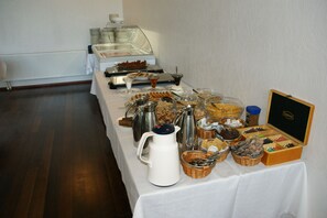 A buffet setup with various food items and beverages, including a coffee station and a box of chocolates.