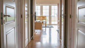 A hallway with wooden floors and white doors leading to a dining area with a table and chairs. - Enjoy Resorts Marina Fiskenæs (Grasten)