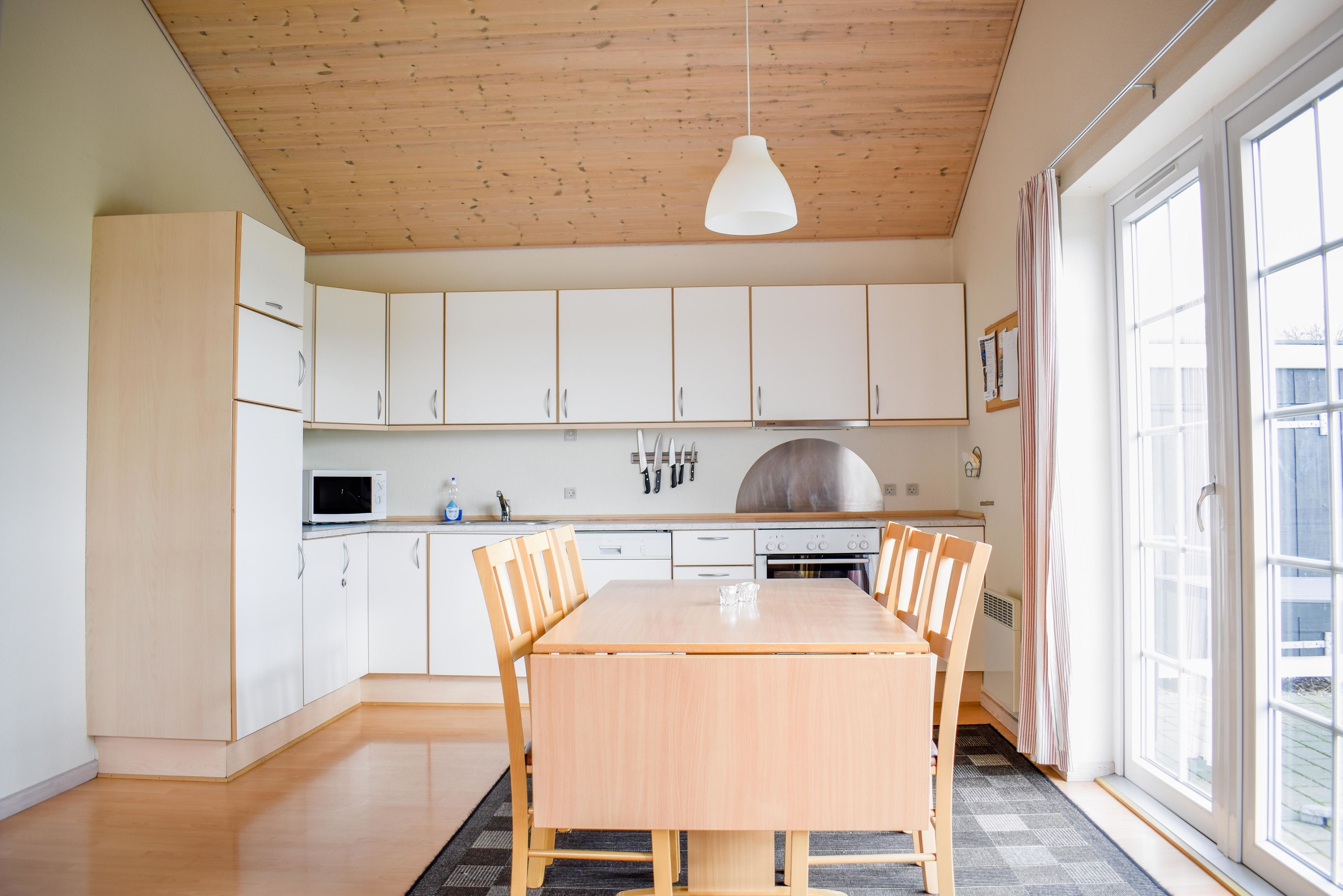 Una cocina moderna con armarios blancos, una mesa de comedor de madera y una lámpara colgante.