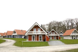 A row of traditional wooden cabins with white railings, a gravel path, and a grassy area in front.