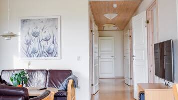 Een ruime woonkamer met een houten plafond, een bank, een salontafel, een televisie en een deur naar een andere kamer.