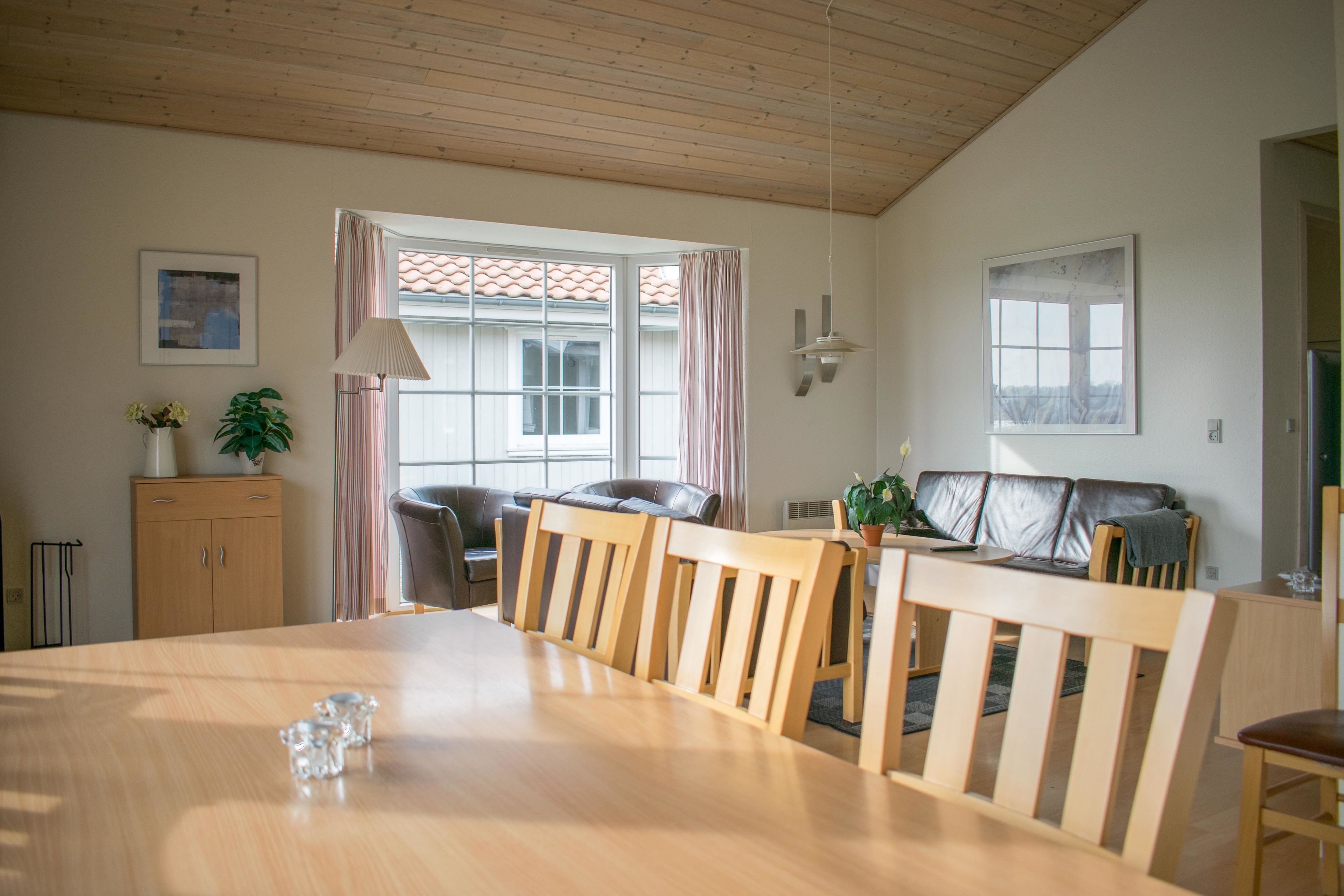 Un área de comedor con una mesa y sillas de madera, un sofá, un armario y una ventana con cortinas.