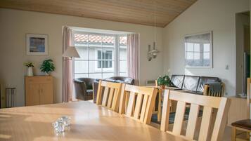 Un área de comedor con una mesa y sillas de madera, un sofá, un armario y una ventana con cortinas.