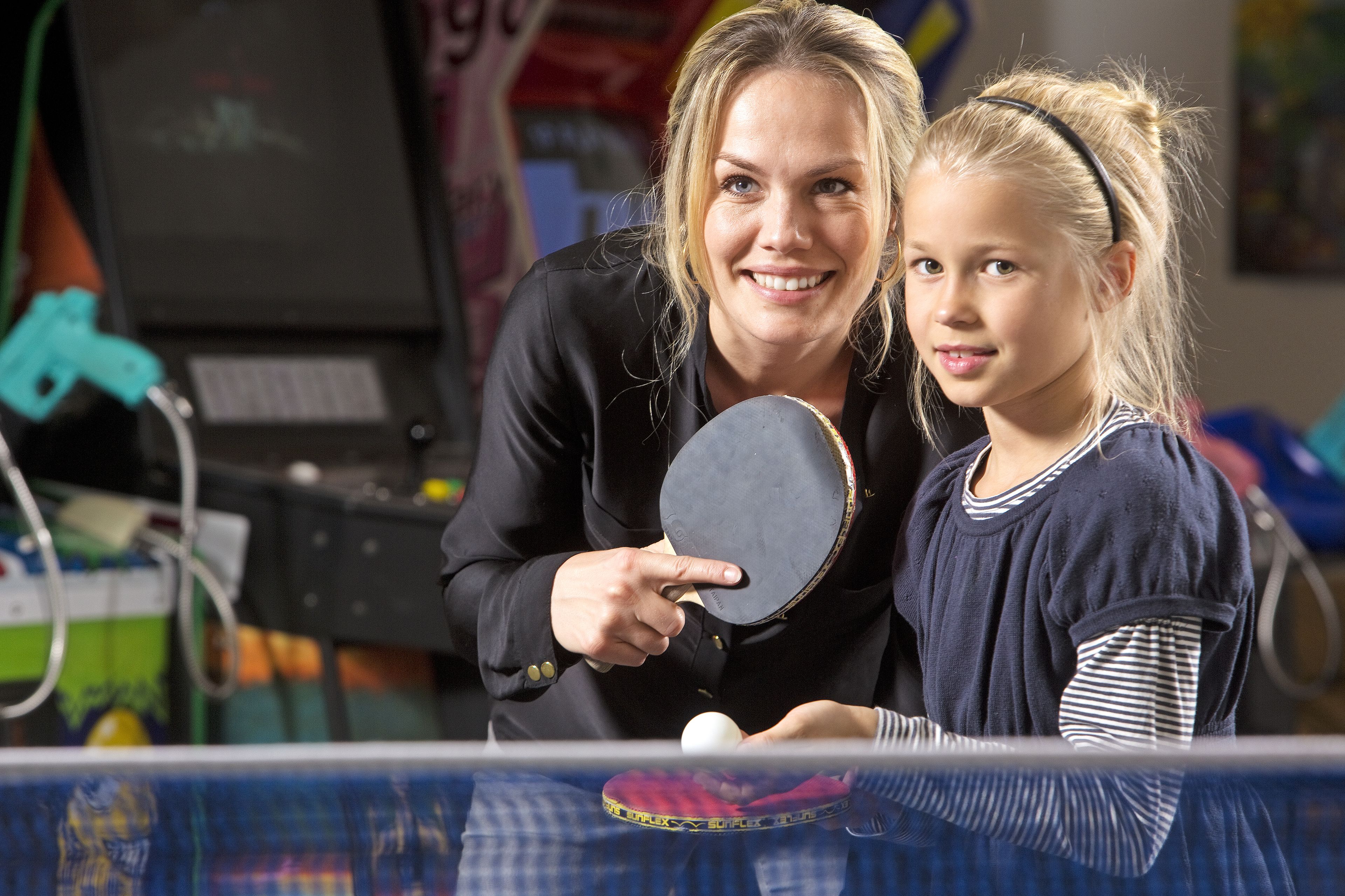 A person holding a ping pong paddle and a ball, with another person standing beside them.