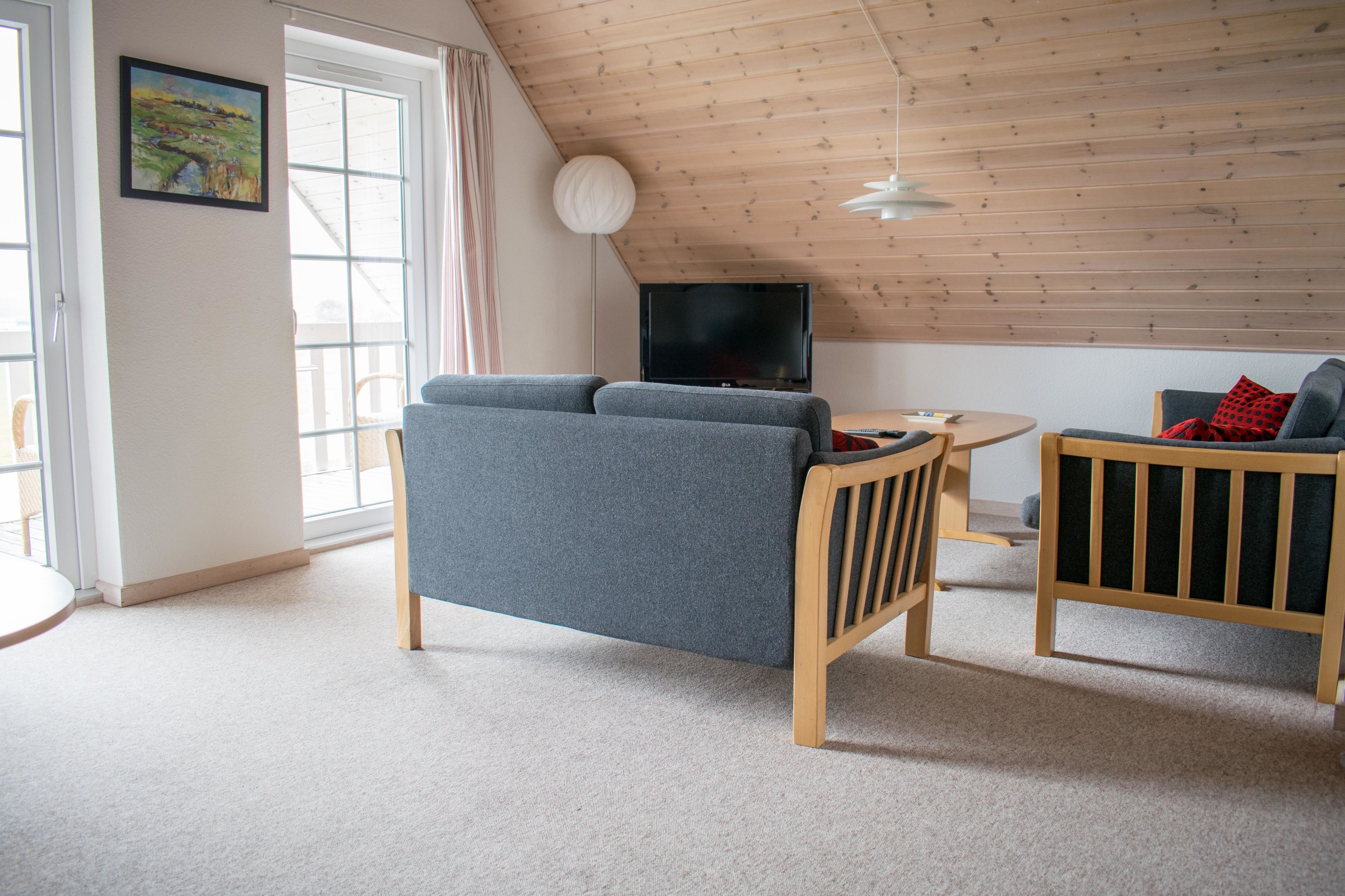A cozy living room with a grey sofa, a wooden chair, a small table, and a TV mounted on the wall.