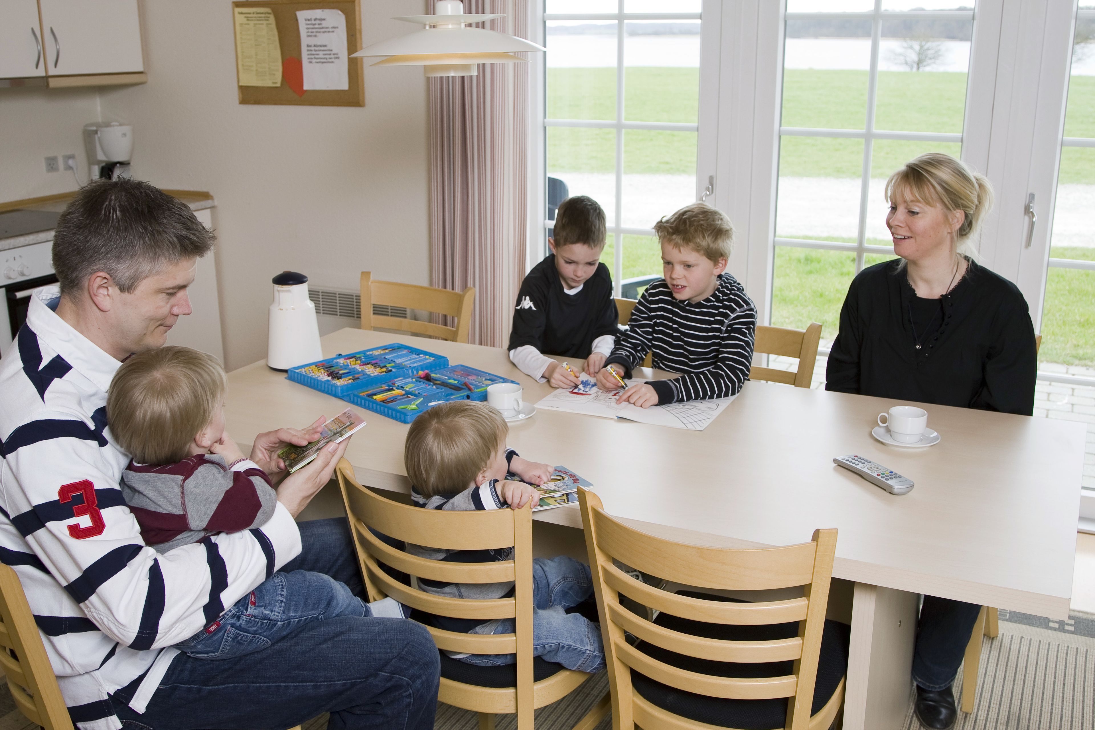 Une famille de cinq personnes est assise autour d’une table, devant un jeu de société, avec une tasse et une télécommande.