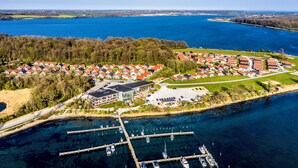 An aerial view of a lakeside residential area with houses, a marina, and a large building with a parking lot. - Enjoy Resorts Marina Fiskenæs (Grasten)