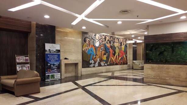 Un vestíbulo moderno con un diseño geométrico en el suelo, un mural grande, una recepción y una zona de estar.