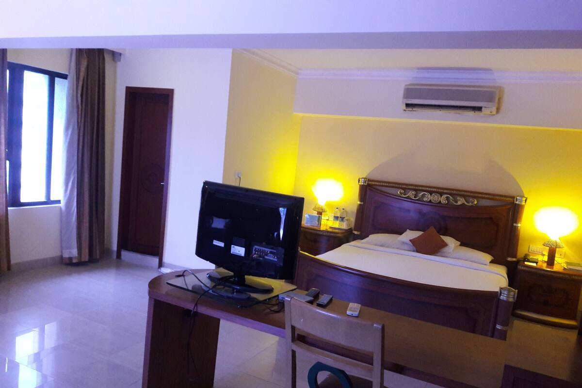 A hotel room with a bed, a desk with a computer, a chair, and bedside lamps.