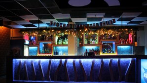Una zona de bar con varias estanterías llenas de botellas, un letrero de neón y una lámpara decorativa.