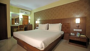 Habitación de hotel con una cama grande, cabecera de madera, mesita de noche con lámpara, escritorio con silla y espejo.