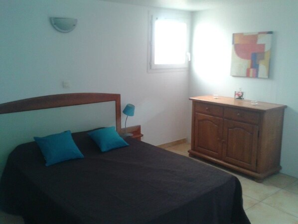 A bedroom with a bed, a nightstand, a wooden cabinet, a wall-mounted light, and a window.