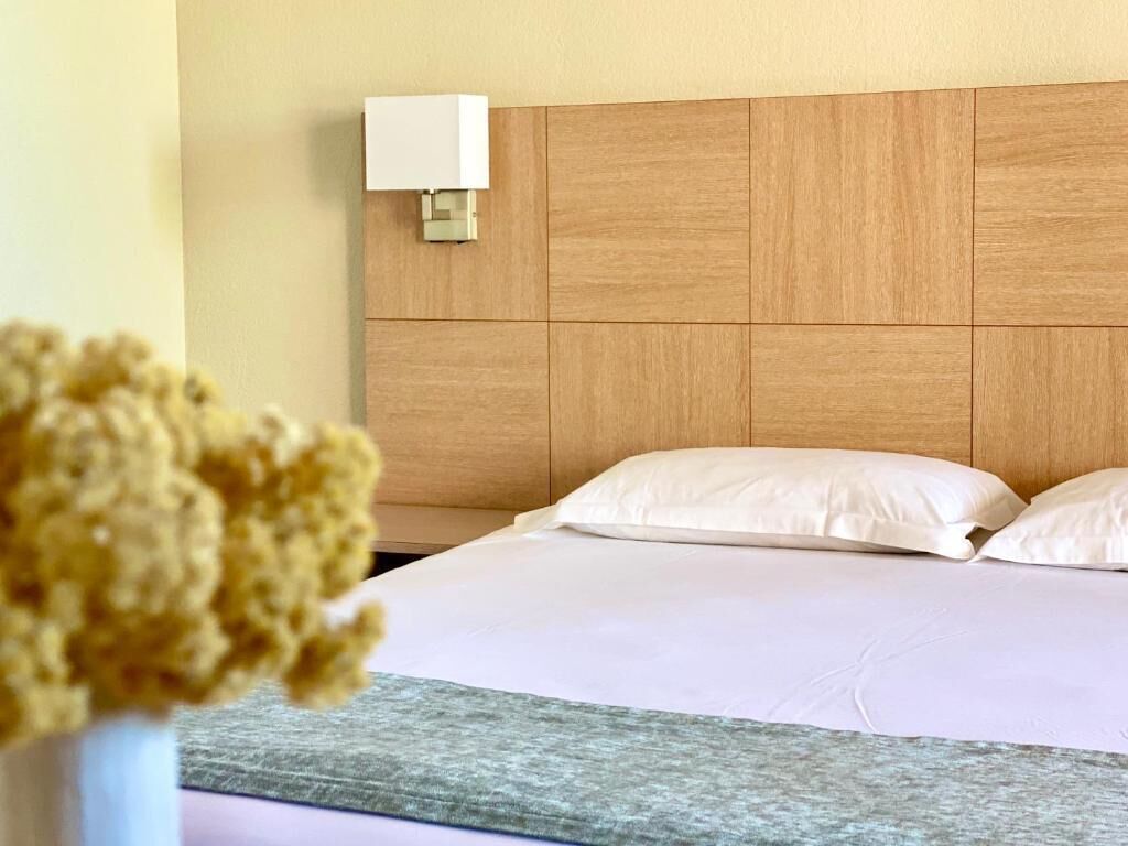 Een hotelkamer met een houten hoofdeinde, witte beddengoed en een wandlamp.