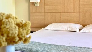 A hotel room with a wooden headboard, white bedding, and a wall-mounted light fixture.