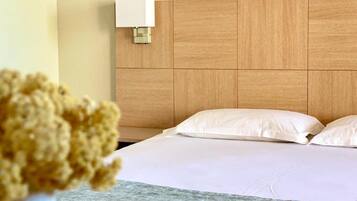Een hotelkamer met een houten hoofdeinde, witte beddengoed en een wandlamp.