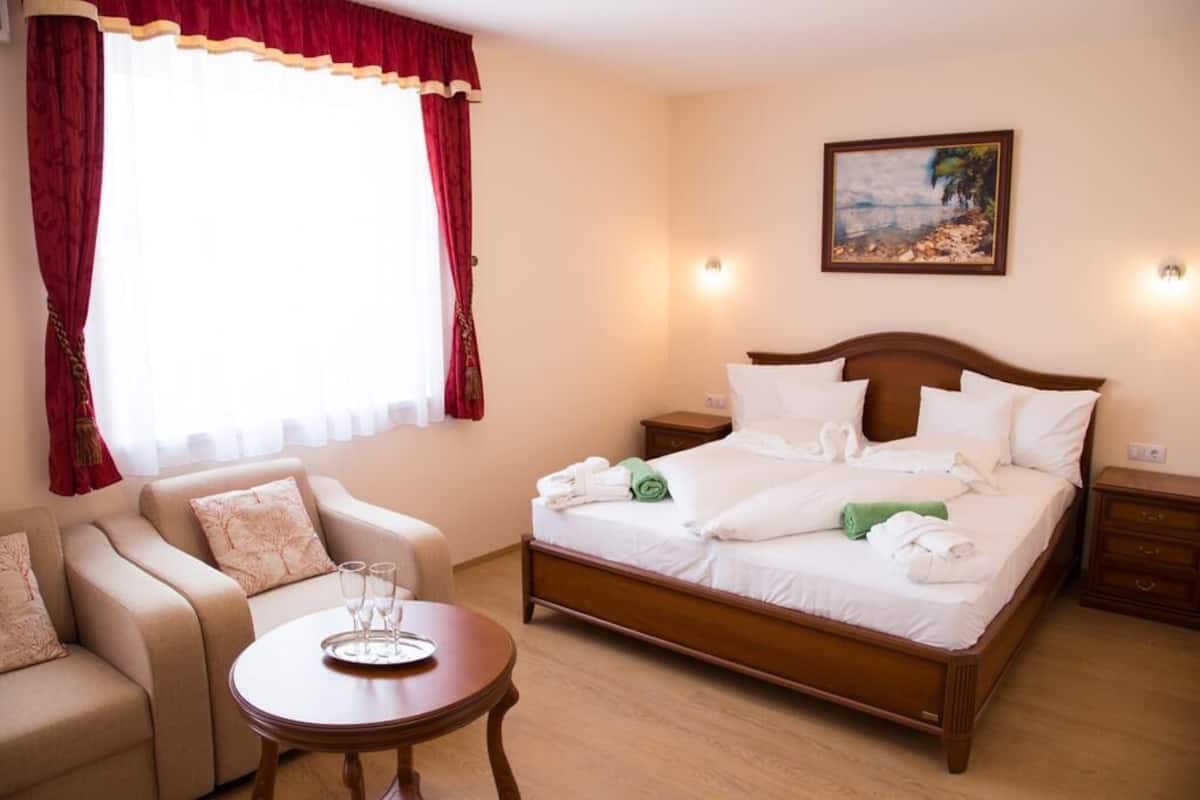 A hotel room with a bed, a sofa, a table, and a painting on the wall.