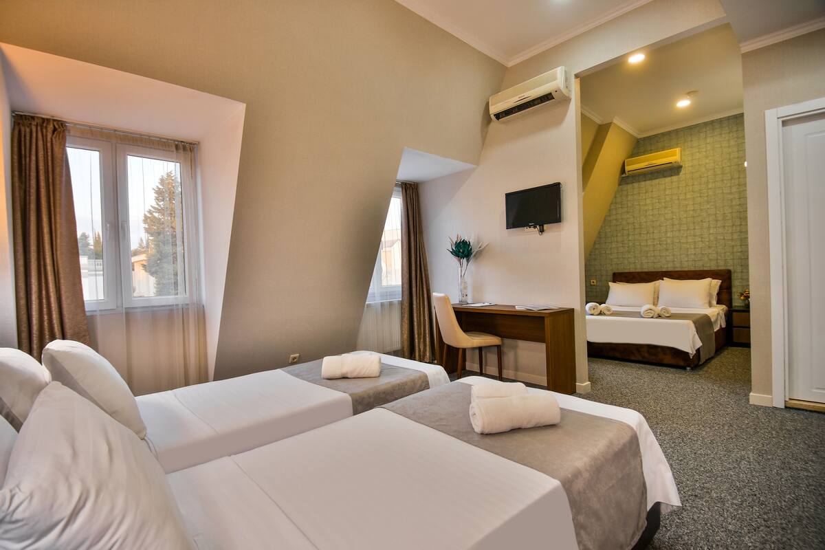 A hotel room with two single beds, a desk, a chair, and a TV on the wall.