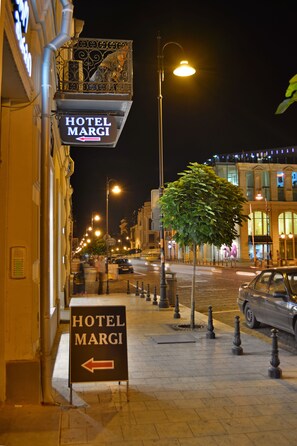 Een straatbeeld bij nacht, met een bordje dat naar links wijst voor 'HOTEL MARGI'.