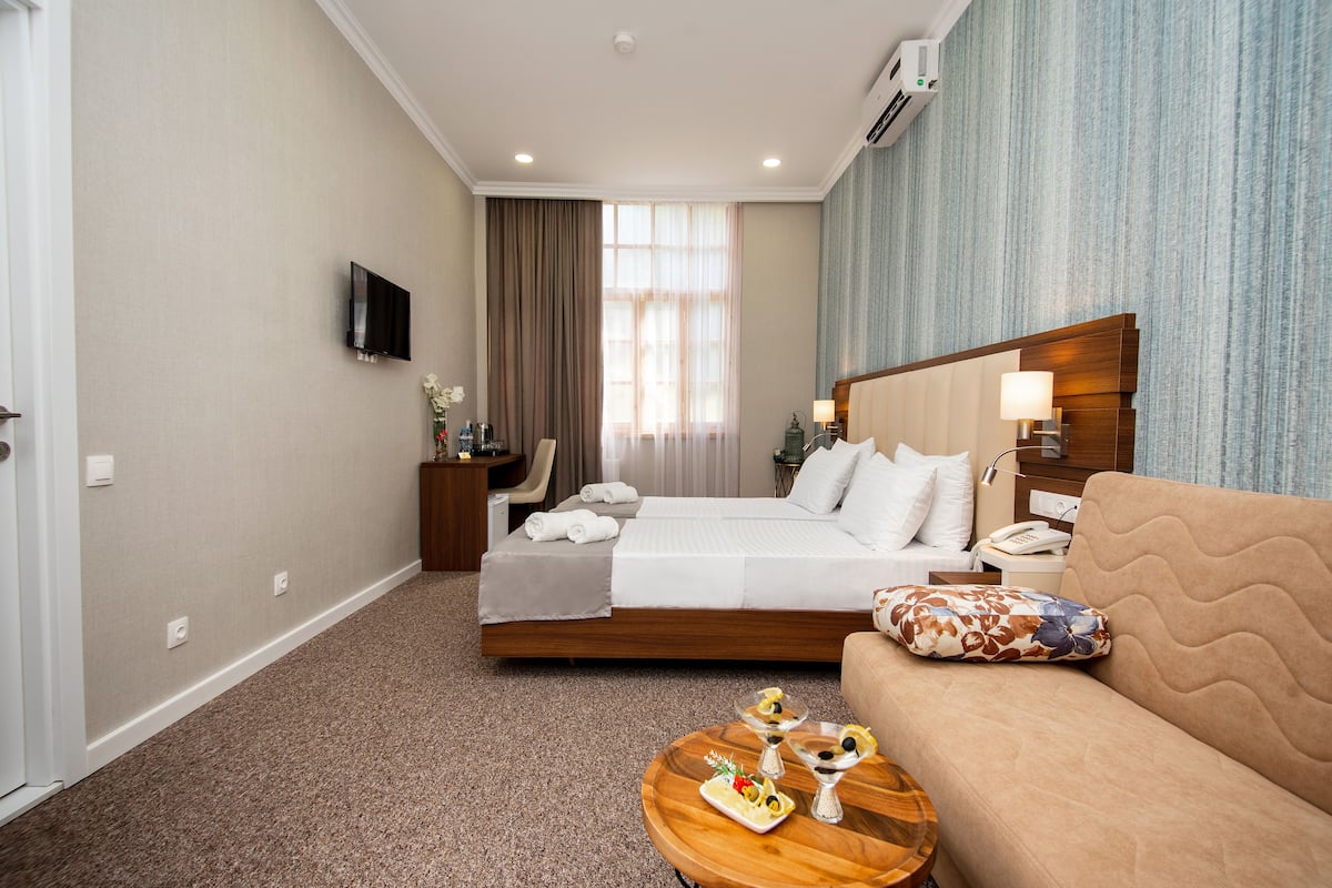 A hotel room with a bed, a sofa, a coffee table, a TV, and a window with curtains.