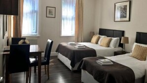 A hotel room with two beds, a desk, and a chair. There are curtains on the windows, and a framed picture on the wall.
