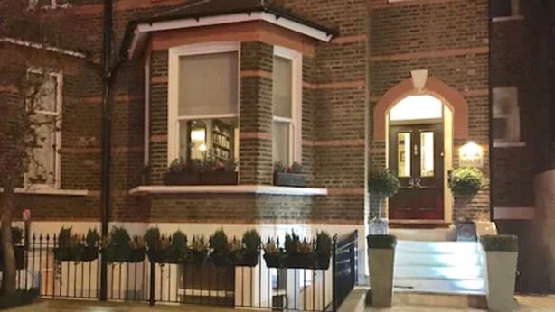 A brick building with a red door and a small balcony with plants.