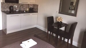 A compact kitchen with white cabinets, a black countertop, and a microwave. There's a small table with a vase and two chairs. A white towel is on the floor.